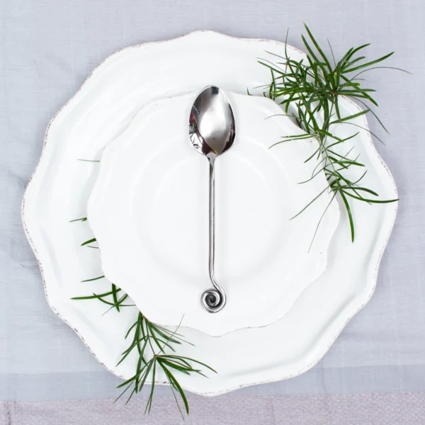 Handcrafted stainless steel teaspoon with scroll handle on white ceramic plate, made in Pilimathalawa Kandy Sri Lanka