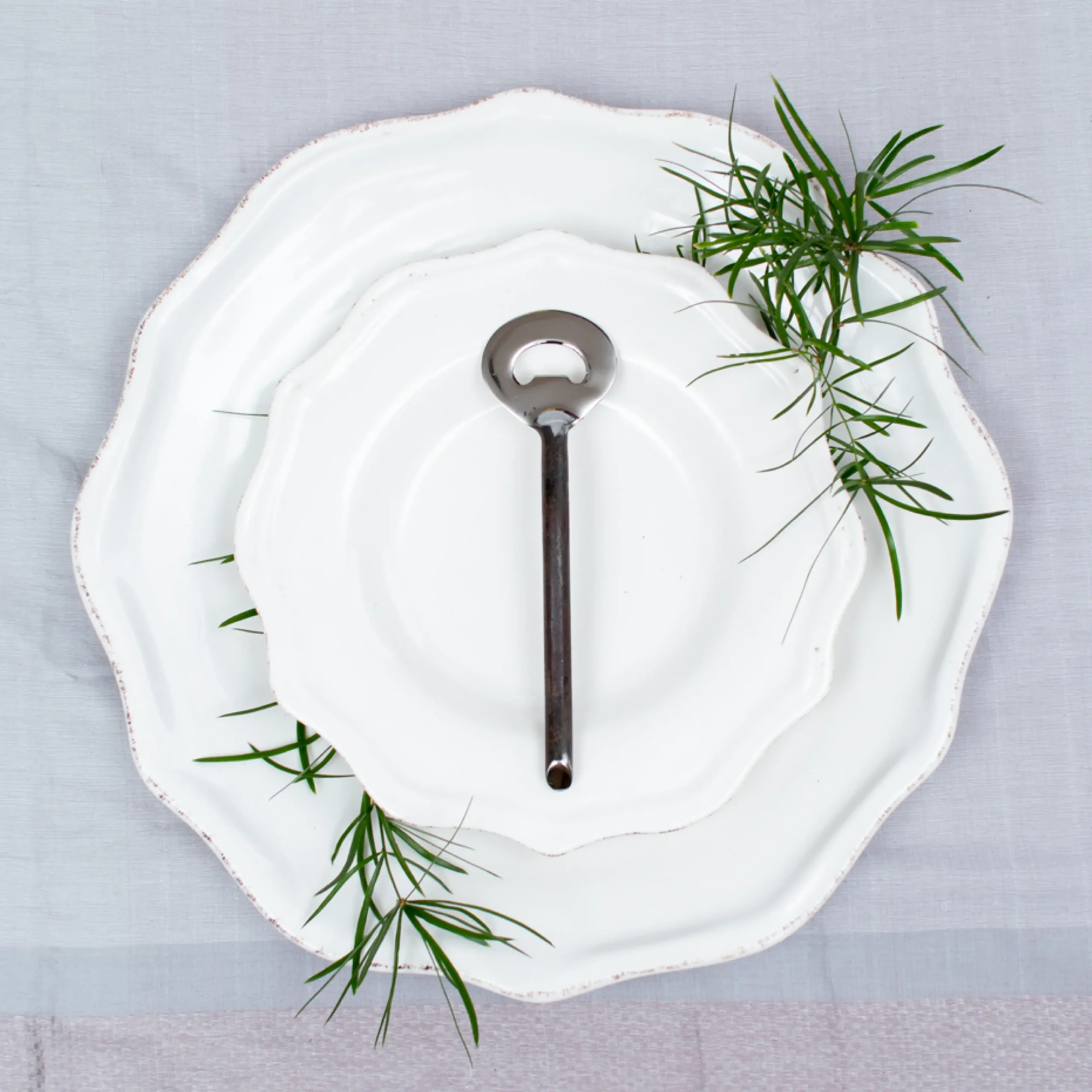 Handcrafted stainless steel bottle opener with oxidised dark handle on white ceramic plate, made in Pilimathalawa Kandy Sri Lanka